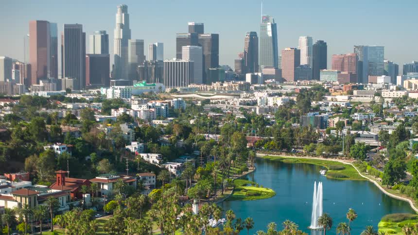 A wide aerial view of a vibrant city skyline with a lake and park in the foreground