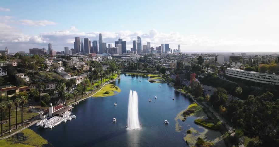 A wide aerial view of a city skyline behind a large park with a lake and palm trees
