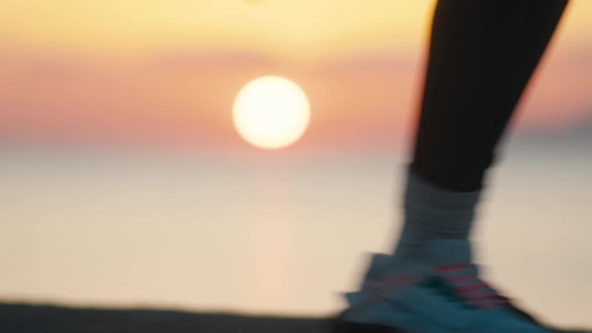 A person wearing sneakers runs on a concrete platform with the rising sun visible in the distance
