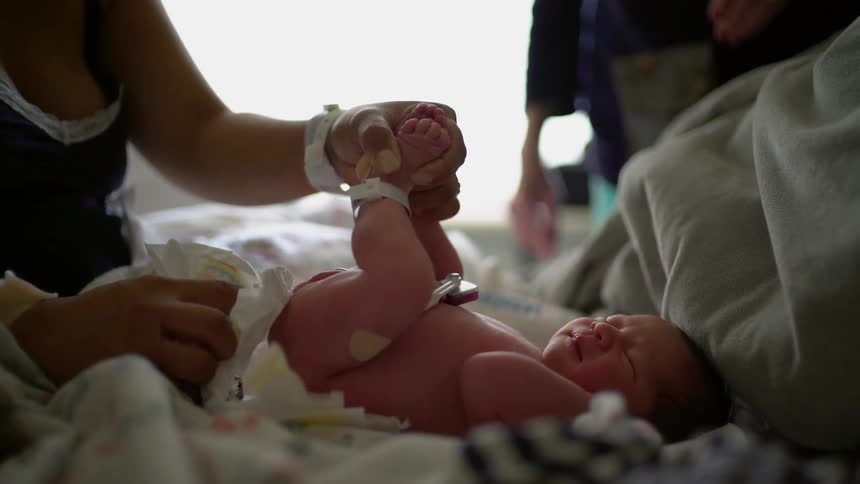 A woman is changing the diaper of a very small baby
