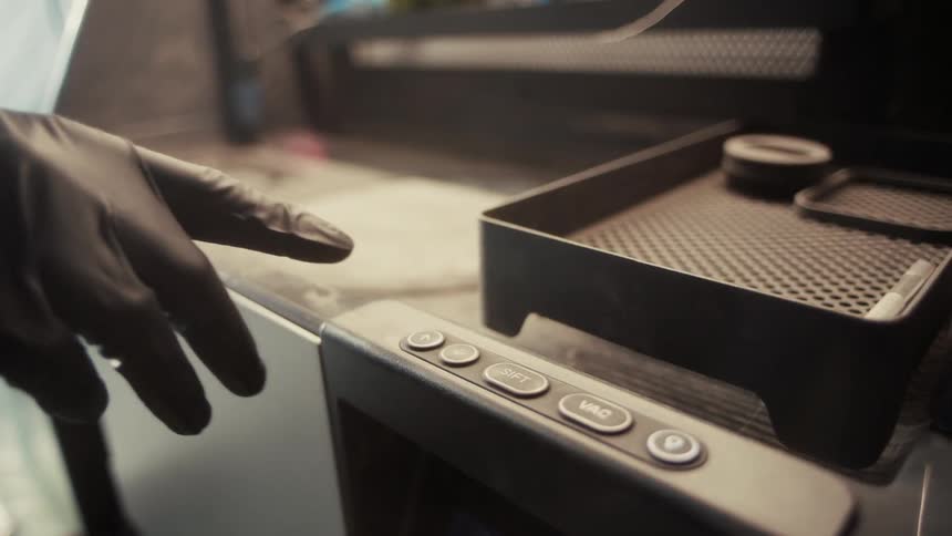 A person wearing gloves presses a button on a machine in an industrial setting