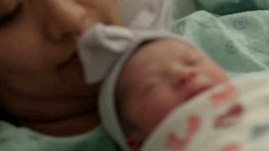 A mother holds a newborn infant to her chest in a hospital bed
