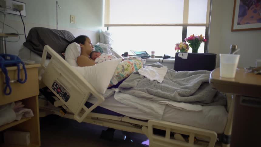 Woman lying in hospital bed with newborn baby on her chest