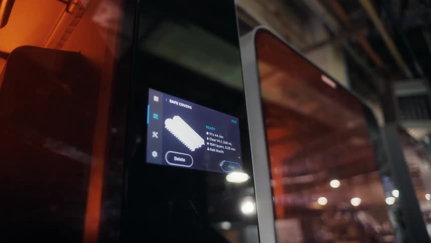 A person interacts with a touch screen on a 3d printing machine to control its operation