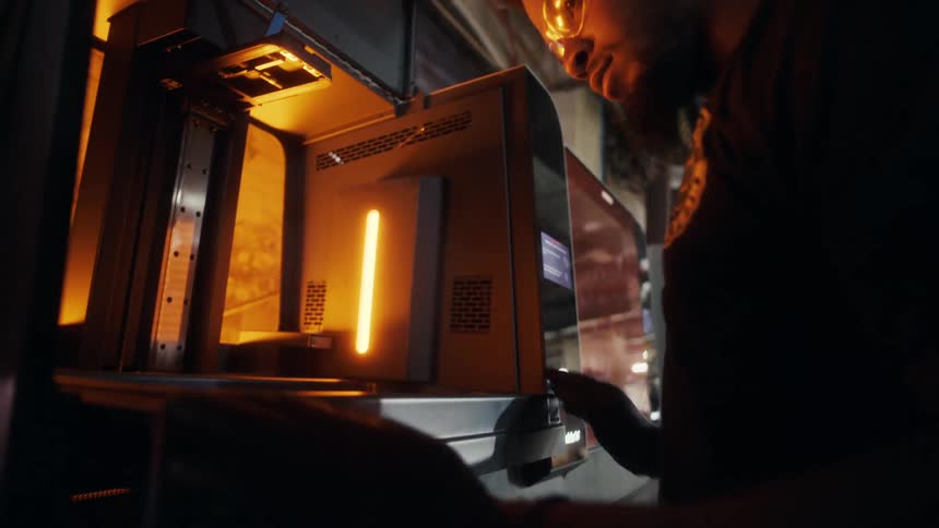A technician adjusts equipment inside a 3d printer in a factory workshop