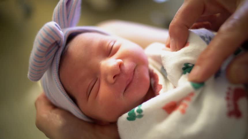 A newborn baby smiles while it is swaddled