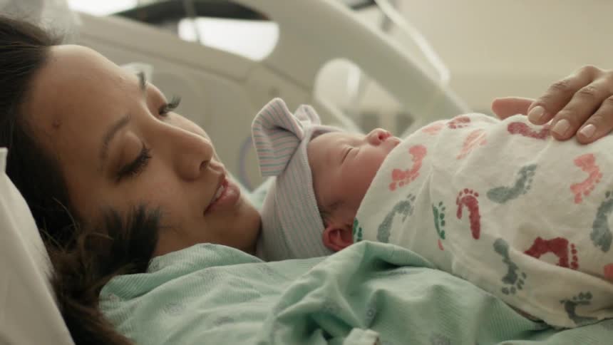 A woman holds a small baby on her chest