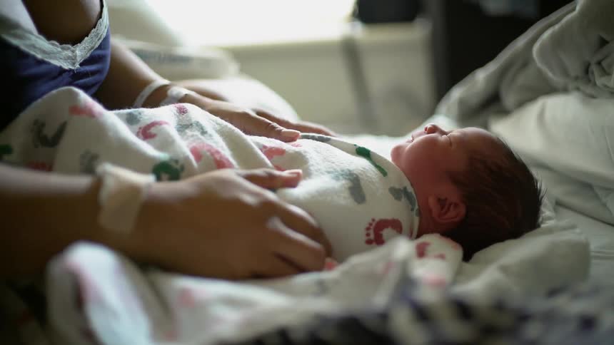 A mother swaddles her newborn in a blanket