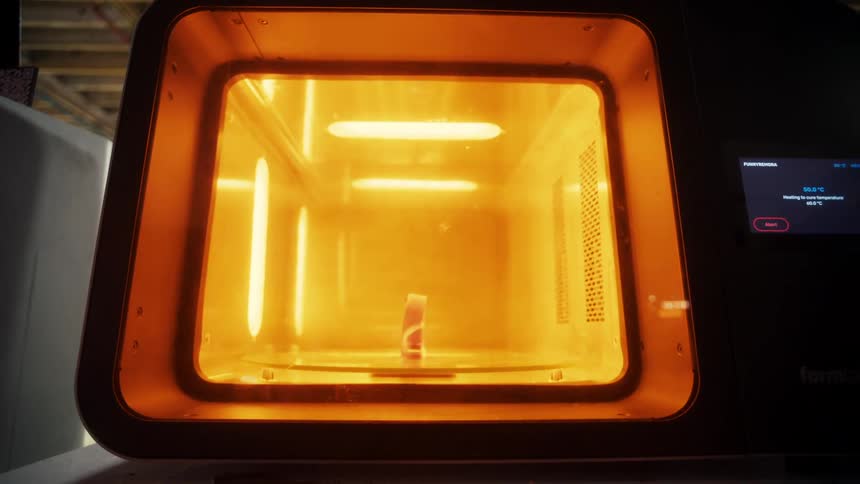 An oven with a glowing interior heats objects inside its chamber while a digital display shows temperature and heating status