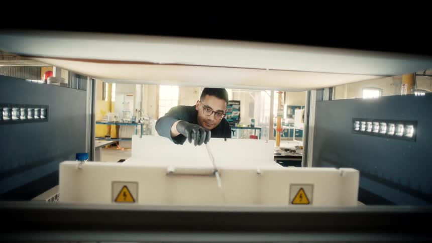 A worker adjusts a piece connected to wires on a white frame inside an industrial machine