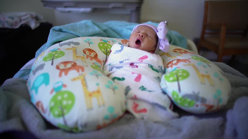 An infant lays swaddled between a pillow