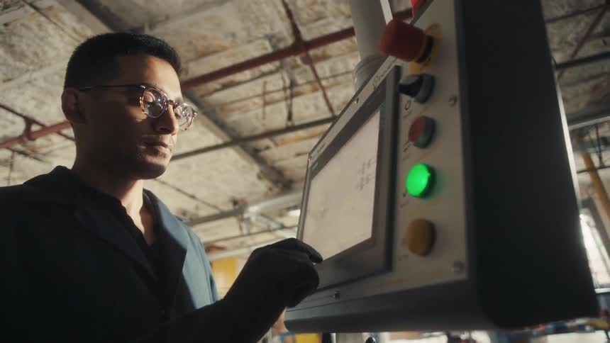 Man standing in a factory interacts with a device with a monitor