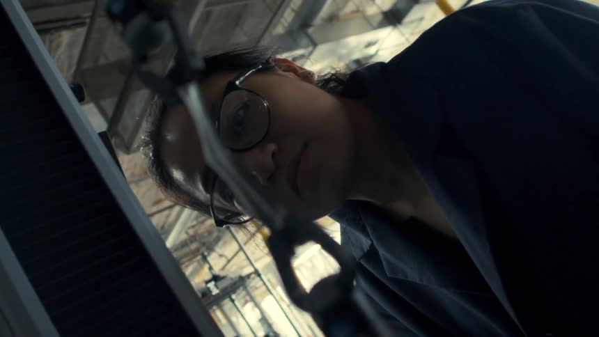 Woman examines an item being manipulated in a manufacturing plant during the daytime