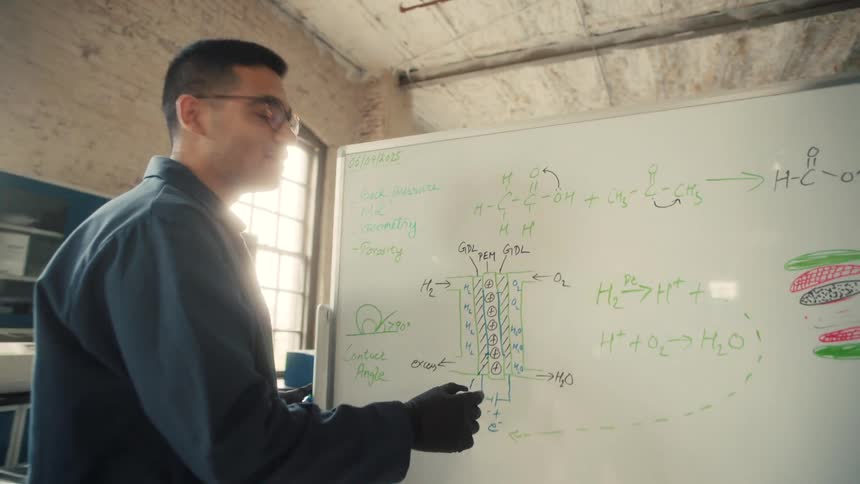 A person points at a whiteboard filled with chemical equations and diagrams related to hydrogen fuel cells and contact angles