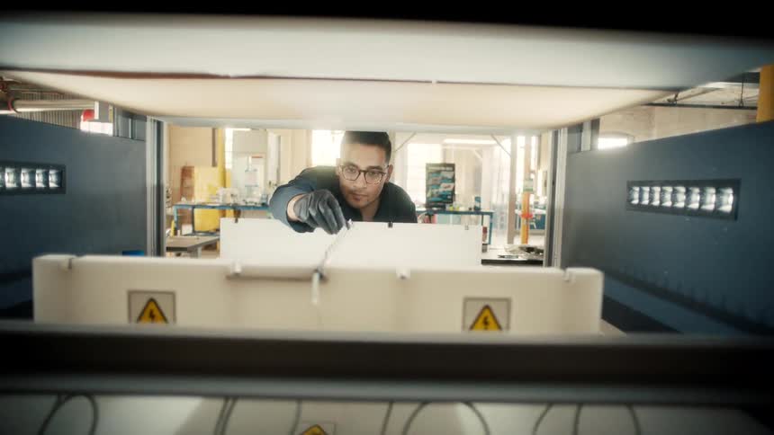 A man operates a large industrial machine inside a well lit factory setting
