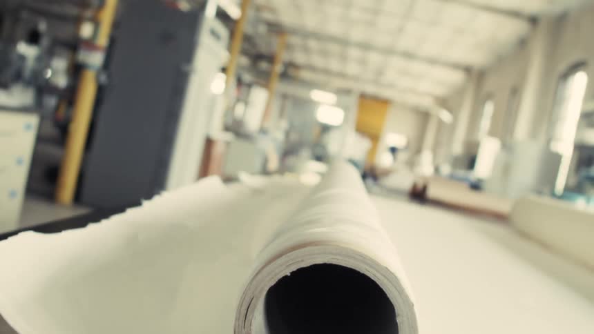 A large roll of white sheet material is placed on a table inside a factory or industrial workspace