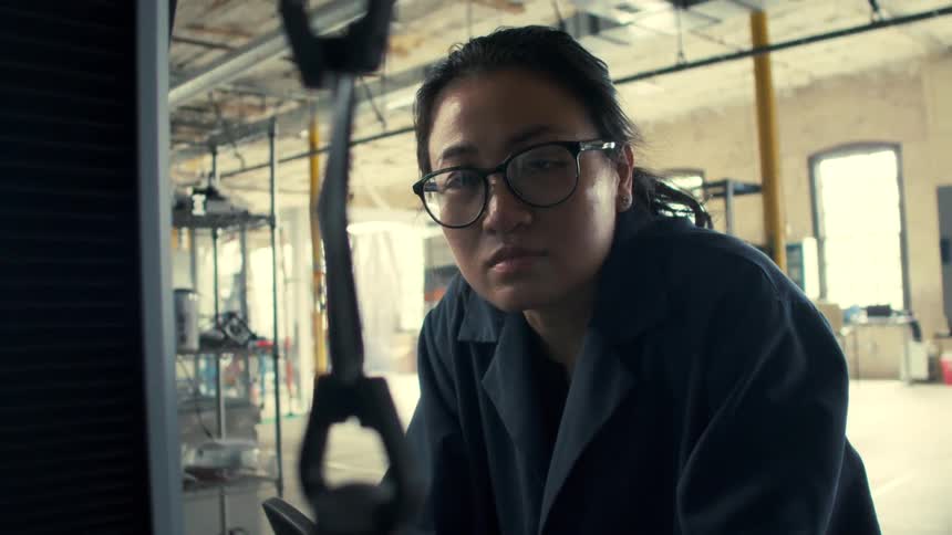 Woman working in a factory observes a part in a machine during the daytime