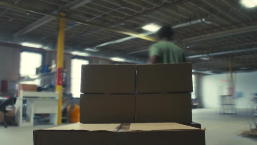A fastpaced timelapse shows a man taping a box and moving a pallet of packages through a busy warehouse