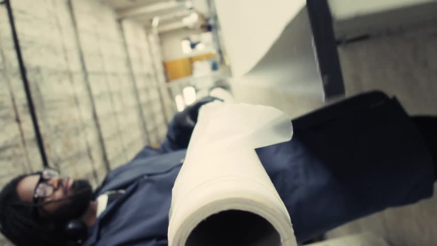 A person carries a large white sheet roller through an industrial hallway