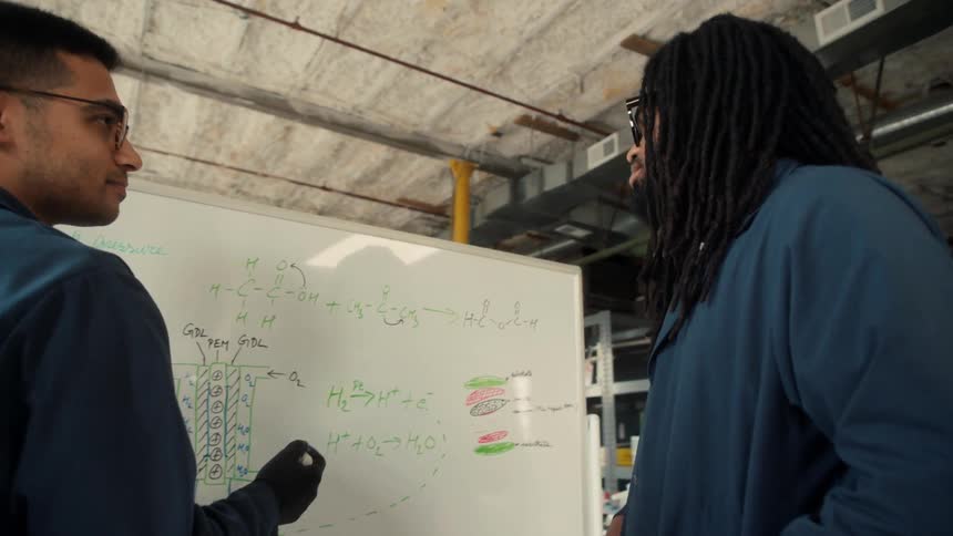 Two men discuss things and write notes on the whiteboard