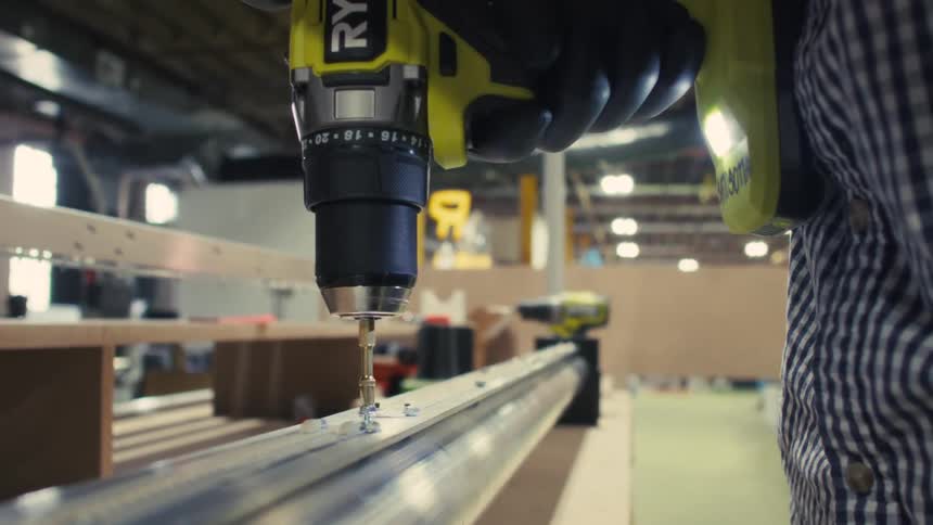 The worker is using a power drill in the factory