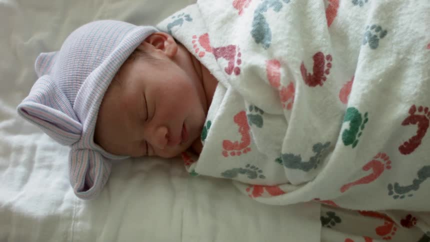A baby wrapped in a blanket lies sleeping