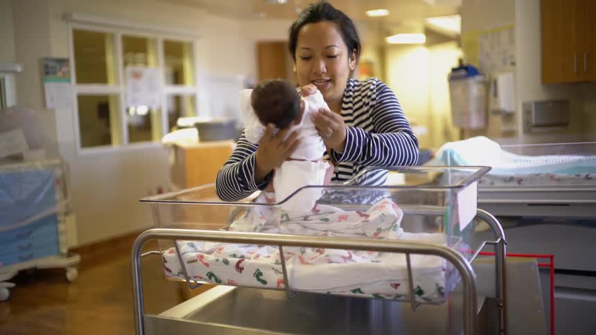 A woman looks at a baby in a crib