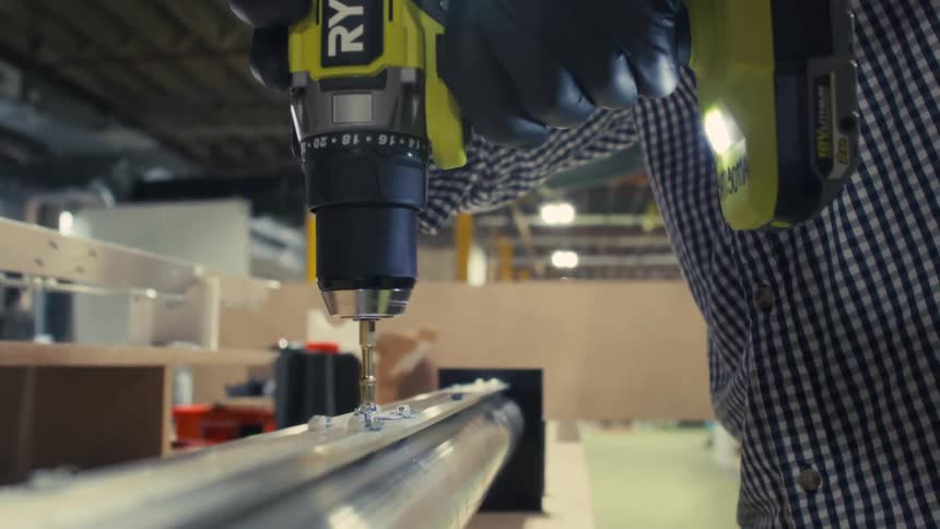 Close up of a male worker using a hand drill to drill a hole into a metal structure in a factory