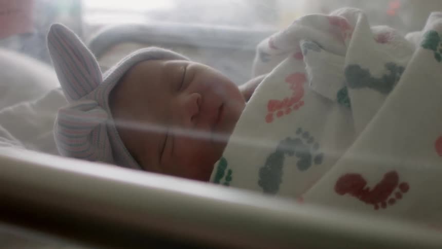 A swaddled newborn lays in a hospital bed