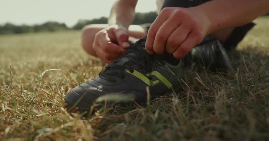 A child is tying their shoe laces outdoors in summer