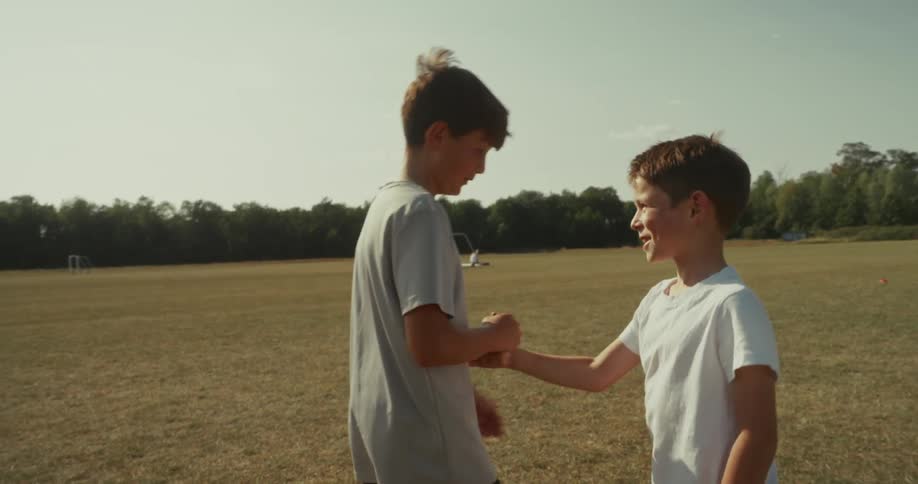 Two boys fist bump each other outdoors in a sunny open field