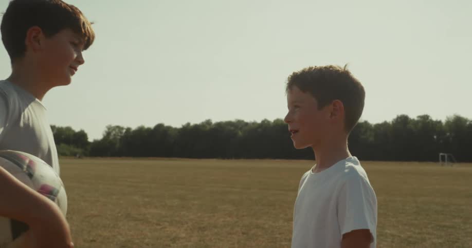 Two friends with one of them holding a soccer ball highfiving each other while standing on an outdoor field