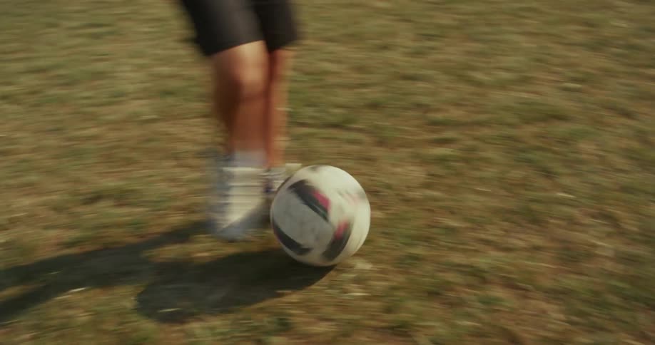 In a fast paced handheld shot the camera follows a soccer ball as its kicked between the feet of two players on a dry grass field