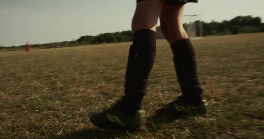 A soccer player dribbles the ball down a field and kicks it towards the goal