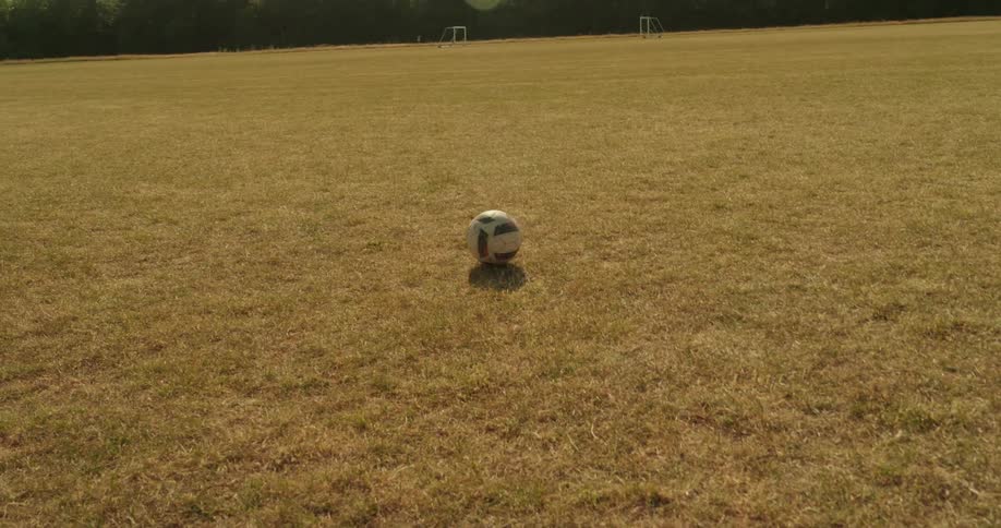 A soccer ball rolls to a stop in the middle of a vast empty sun drenched field