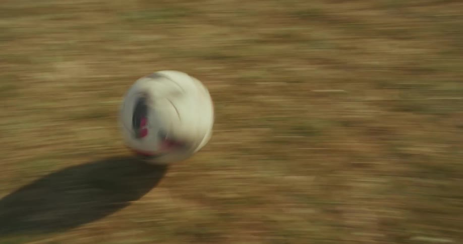 Two people are kicking a soccer ball back and forth between themselves on a field at midday