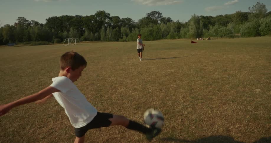 Two kids are playing a game of soccer in an empty field