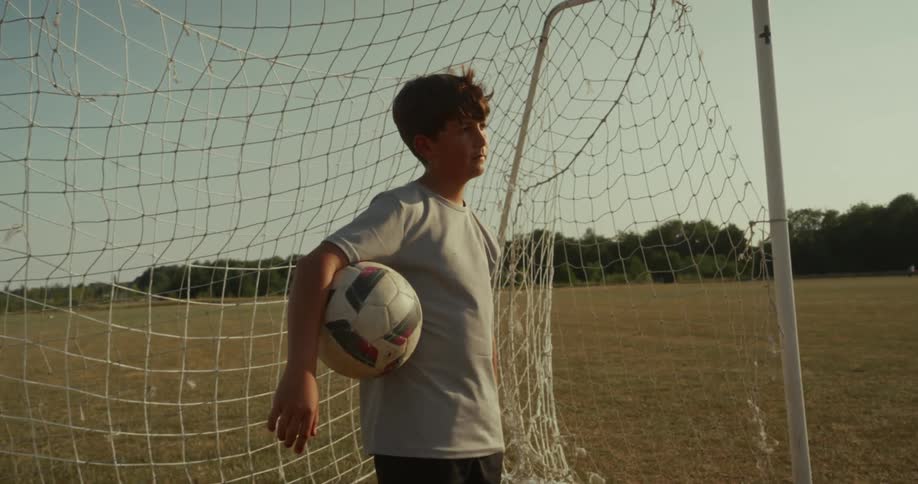 A boy is standing in front of a soccer net outdoors