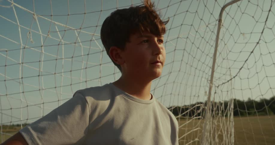 A boy is standing in front of a soccer net on an outdoor field
