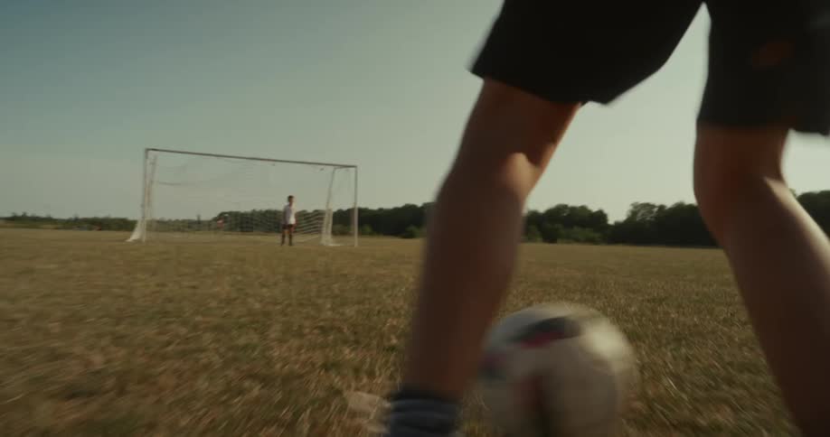 A kid is kicking a soccer ball into the soccer net