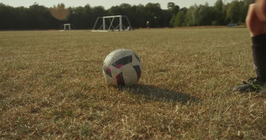 A boy places a soccer ball on the grass in the park