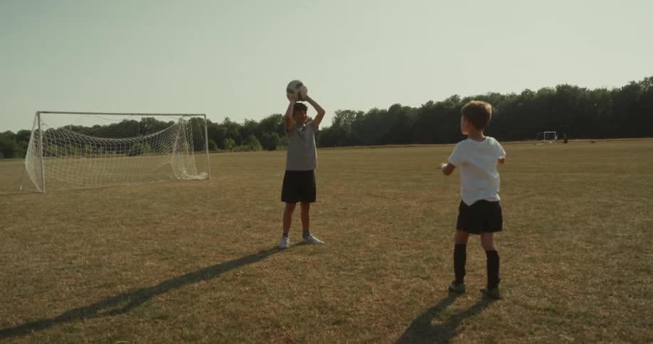 Two kids are playing a game of catch with a soccer ball