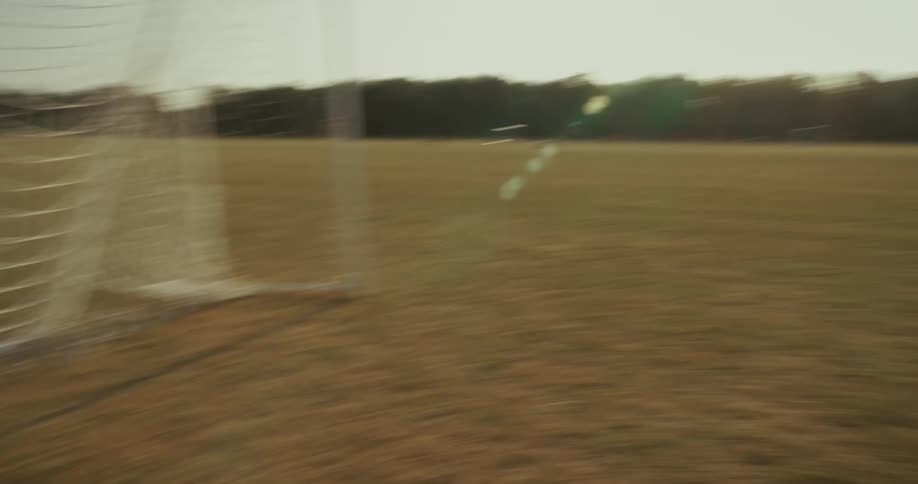 A young boy in a white tshirt standing on a grassy field possibly a soccer field looking around the camera then quickly pans creating a blurry effect across the field