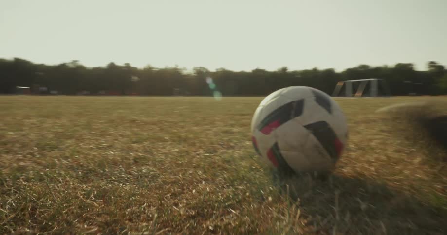 A child kicks a soccer ball toward the goal on a sunlit dry field