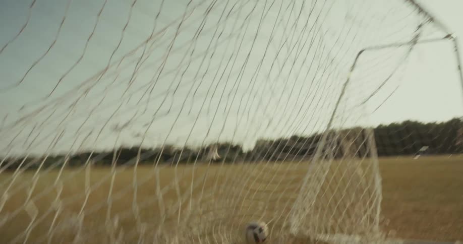 Boy playing soccer and kicking a ball and scoring a goal in an open air field