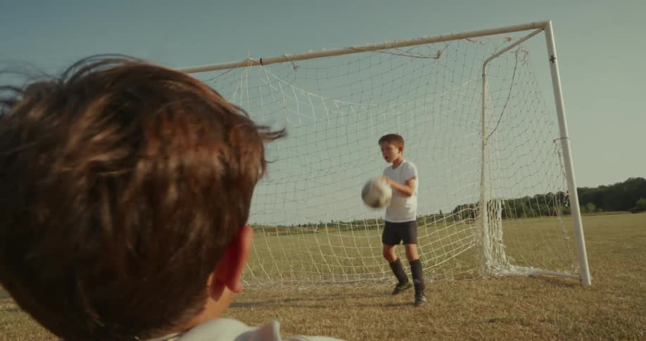 Two boys playing soccer on a sunny field with one boys back of the head visible in the foreground suggesting a firstperson perspective or closeup shot from another player the boy in the background is actively engaged in the game