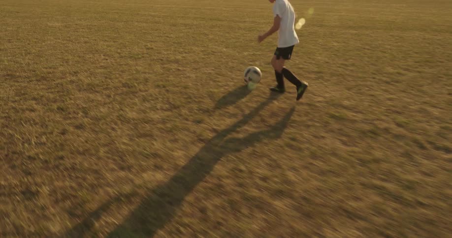 Boy dribbles a soccer ball across the field before kicking it into the goal on a summer day