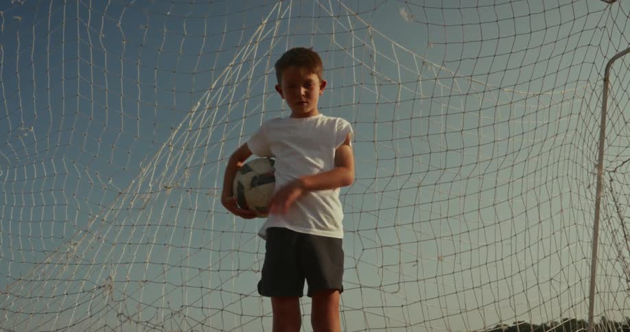 Boy in a goal with a net holding a soccer ball