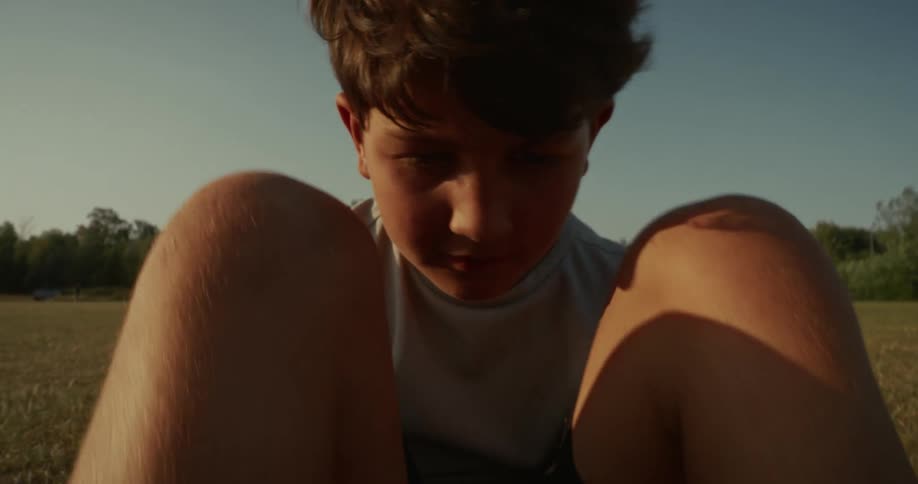 A boy performs crunches on a grassy field curling their torso upward with knees bent and arms raised