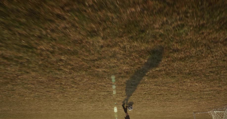 A child kicks a soccer ball toward the net on a dry patchy field